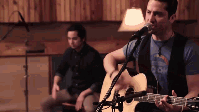 a man singing into a microphone while another man plays a guitar in the background