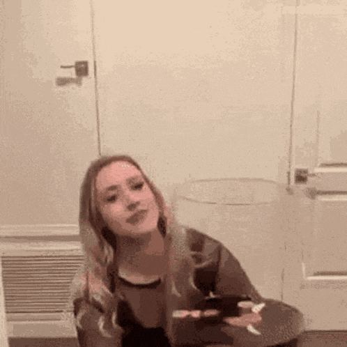 a woman is sitting at a table in front of a door holding a cigarette .