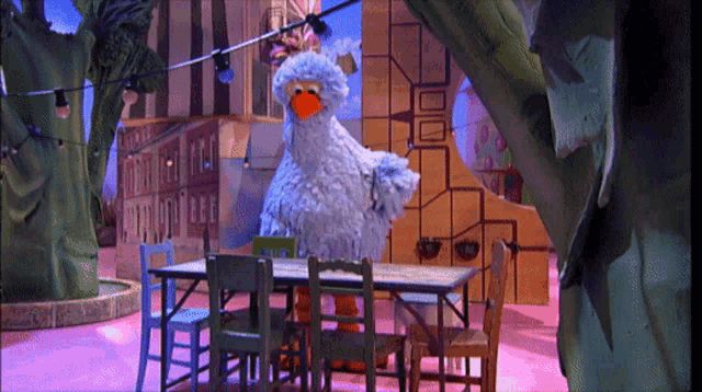 sesame street big bird is standing next to a table with chairs