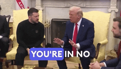 a man sitting next to a man in a suit and tie with a sign that says you 're in no