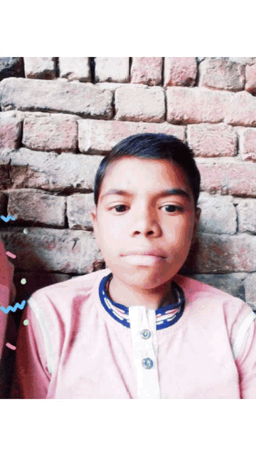 a young boy wearing a pink shirt stands in front of a brick wall