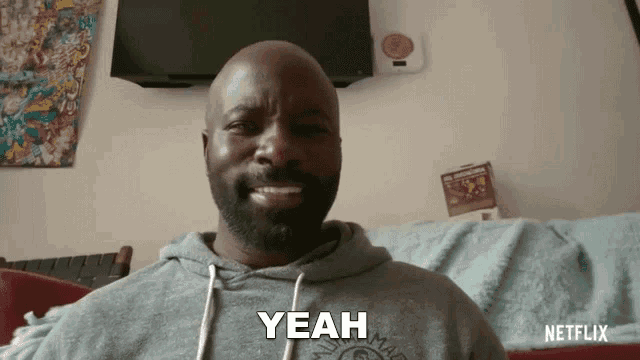 a bald man with a beard is sitting on a couch and saying yeah