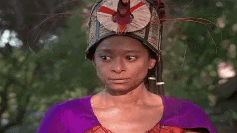 a woman wearing a purple dress and a feathered hat is looking at the camera .
