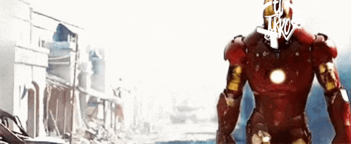a man in an iron man suit is standing in front of a destroyed building .