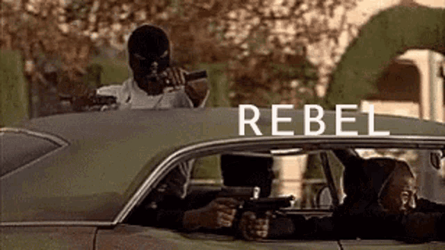 a man in a mask is holding a gun in a car with the word rebel on the roof .