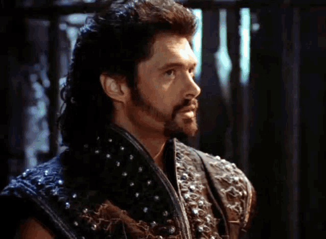 a man with a beard is wearing a black leather vest with studs