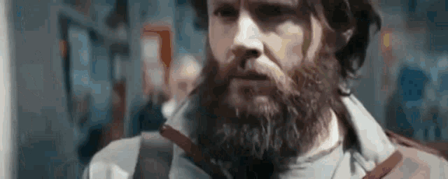 a man with a beard and long hair is standing in a crowded area .