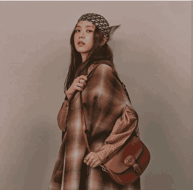 a woman wearing a plaid coat is holding a brown purse