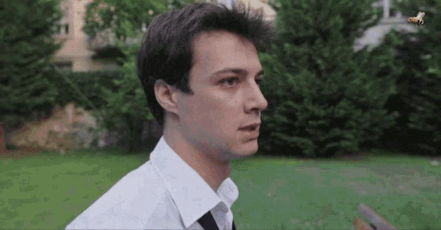 a man in a white shirt and tie stands in front of trees