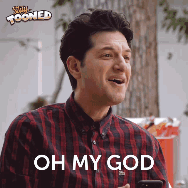 a man in a plaid shirt is holding a cell phone and says " oh my god "