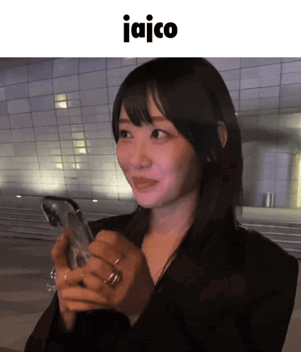 a woman holding a cell phone in front of a building that says jaico on it