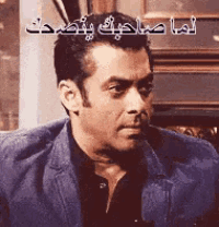 a man in a suit and black shirt is looking at the camera with arabic writing behind him .