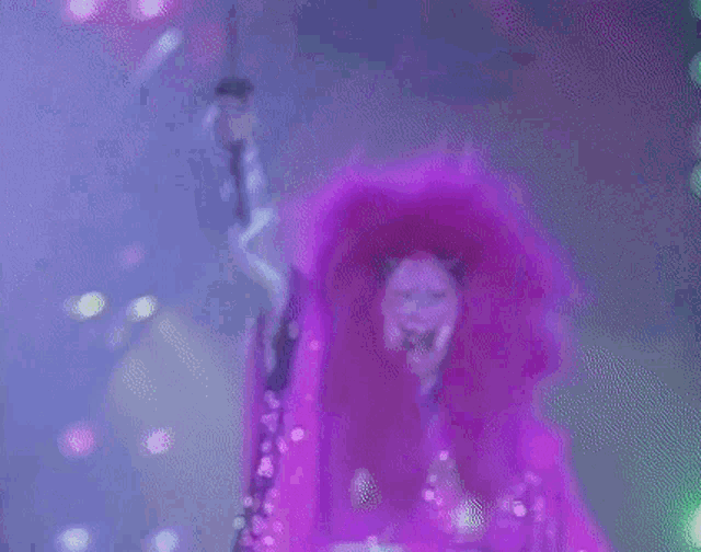 a woman in a purple fur coat is holding a microphone in her hand .