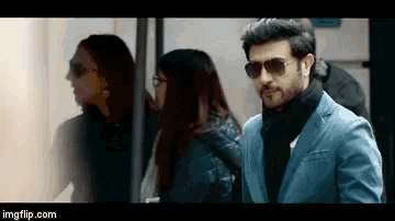 a man wearing sunglasses and a blue jacket is standing next to a woman .