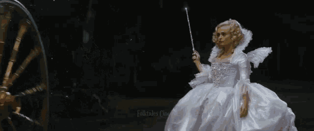 a woman in a white dress is holding a wand in front of a carriage wheel .