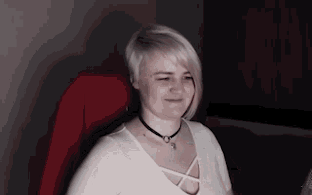 a woman wearing a white shirt and a black choker smiles