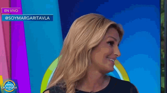 a woman is smiling in front of a sign that says en vivo @soymargaritavla