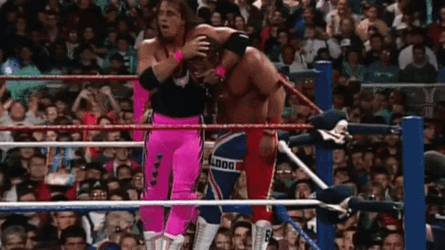 a wrestler in a pink outfit is standing in a wrestling ring with a crowd watching