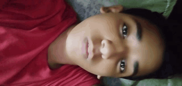 a young man in a red shirt is laying down on a bed .