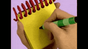 a person is writing on a yellow notebook with a green pen