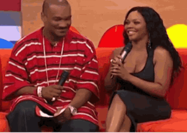 a man in a red striped shirt sits next to a woman in a black dress who is holding a microphone