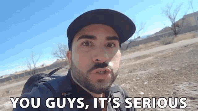 a man with a beard wearing a hat and a backpack says you guys it 's serious