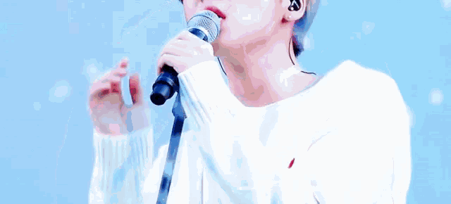 a young man is singing into a microphone while wearing a white sweater .