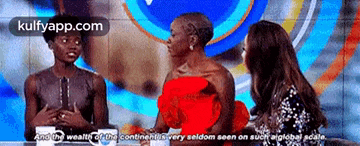 a woman in a red dress is talking to two other women on a stage .