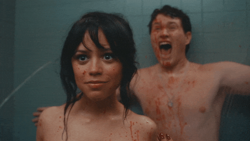 a woman with blood on her face smiles next to a shirtless man with blood on his face