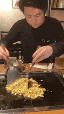 a man wearing a black shirt with the letter u on it is cooking food