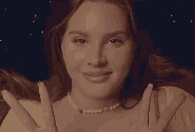 a woman wearing a yellow shirt and a pearl necklace holds her hands up
