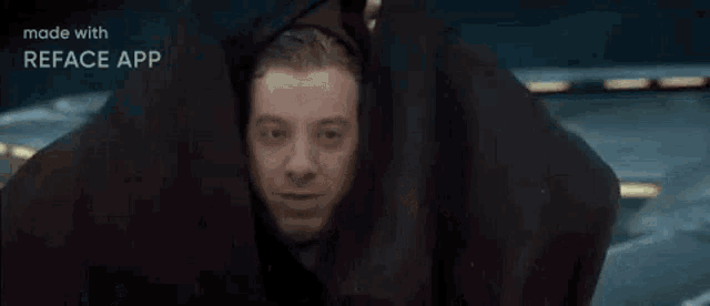 a man with a beard and a hooded jacket is sitting in a room .