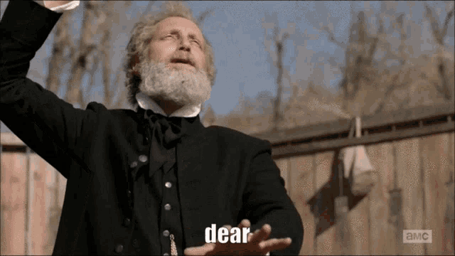 a man with a beard and a black suit says dear