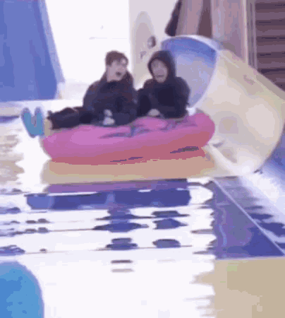 two people are riding a pink inflatable raft down a water slide at a water park .
