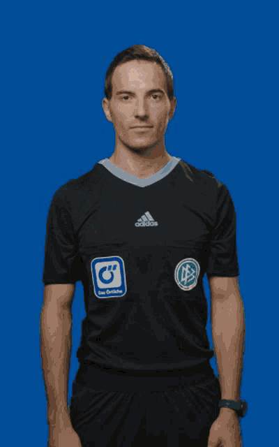 a man wearing a black adidas shirt stands in front of a bright blue background
