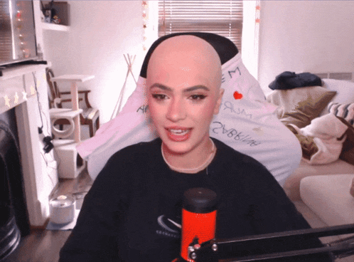 a woman with a shaved head sits in front of a microphone with the word em on her shirt