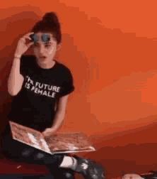 a woman wearing a black shirt that says future is female is reading a book
