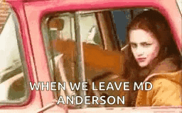 a woman is sitting in the driver 's seat of a pink truck and looking out the window .