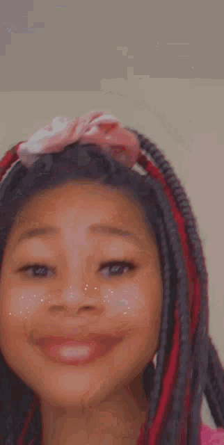 a young girl with red braids and a pink headband is smiling for the camera .
