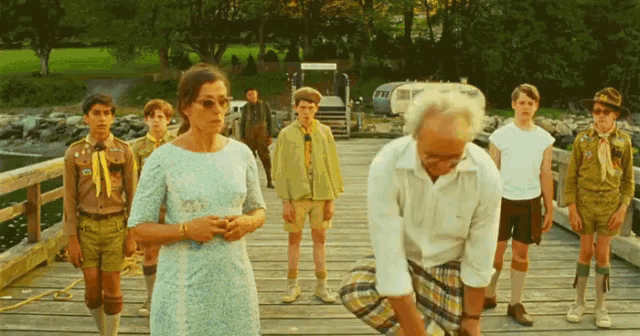a group of people standing on a wooden bridge including a man wearing sunglasses
