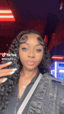 a woman with long curly hair and white nails is wearing a black jacket and a denim jacket .