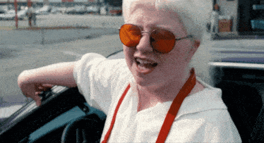 a woman wearing red sunglasses and red suspenders is driving a car