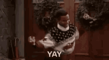 a man in a sweater is dancing in front of a door with the word yay .