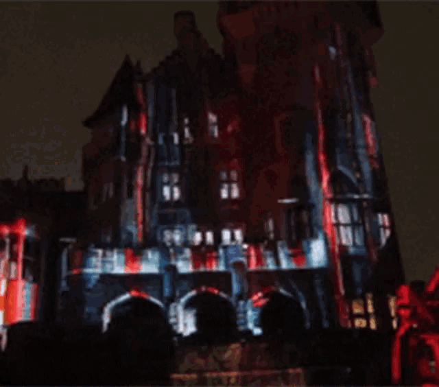 a castle is lit up at night with red and blue lights projected on it