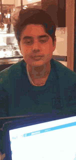 a man in a green sweater is sitting in front of a computer screen with his eyes closed