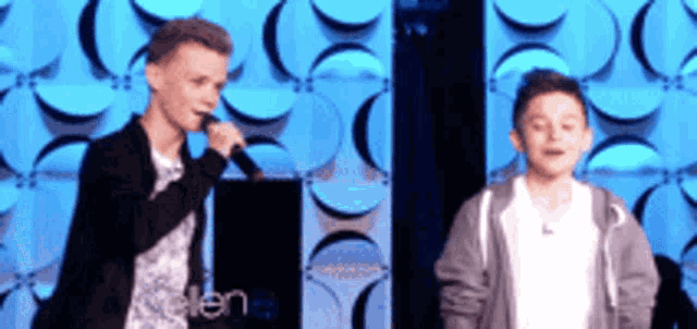 two boys are singing into microphones in front of a ellen degeneres sign