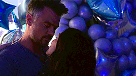 a man and a woman are standing next to each other in front of a bunch of blue balloons .