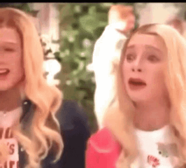 two blonde women are standing next to each other and one is crying while the other is smiling .