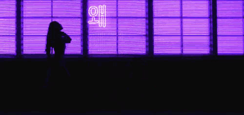 a woman is standing in front of a purple neon sign that says ' a ' on it