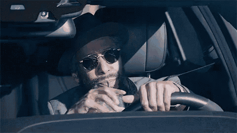 a man with a beard and sunglasses is driving a car